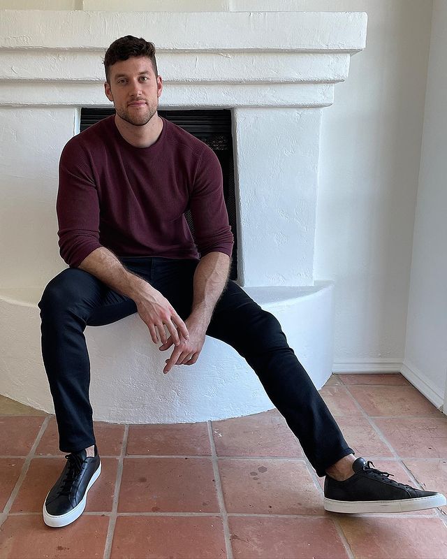 Clayton Echard in a maroon sheatshirt and black pants with white soled black shoes.